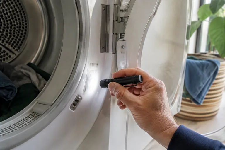 Hand met zaklamp bij het typeplaatje van een wasapparaat