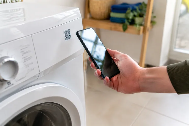 Smartphone in de hand naast een wasapparaat