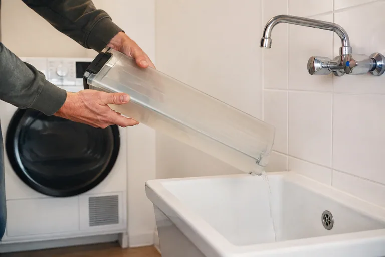 Water uit het condensreservoir van een droger wordt in een gootsteen gegoten