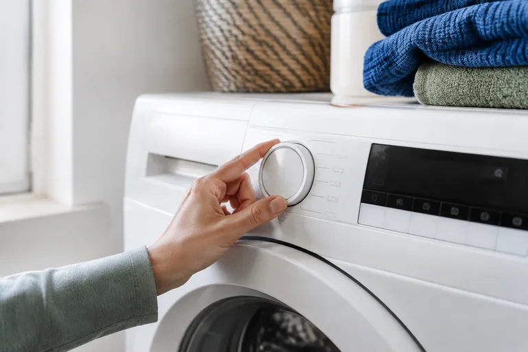 Hand bij de programmaknop van een wasmachine