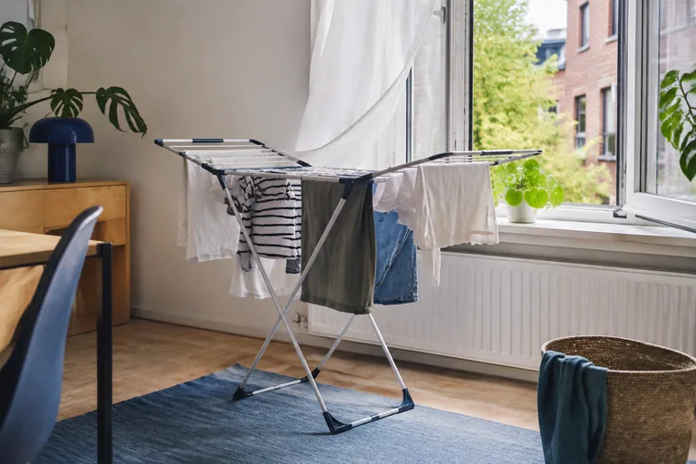 Kleding droogt op een wasrek bij een open raam