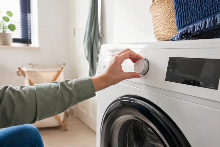 Hand bij de programmaknop van een wasmachine