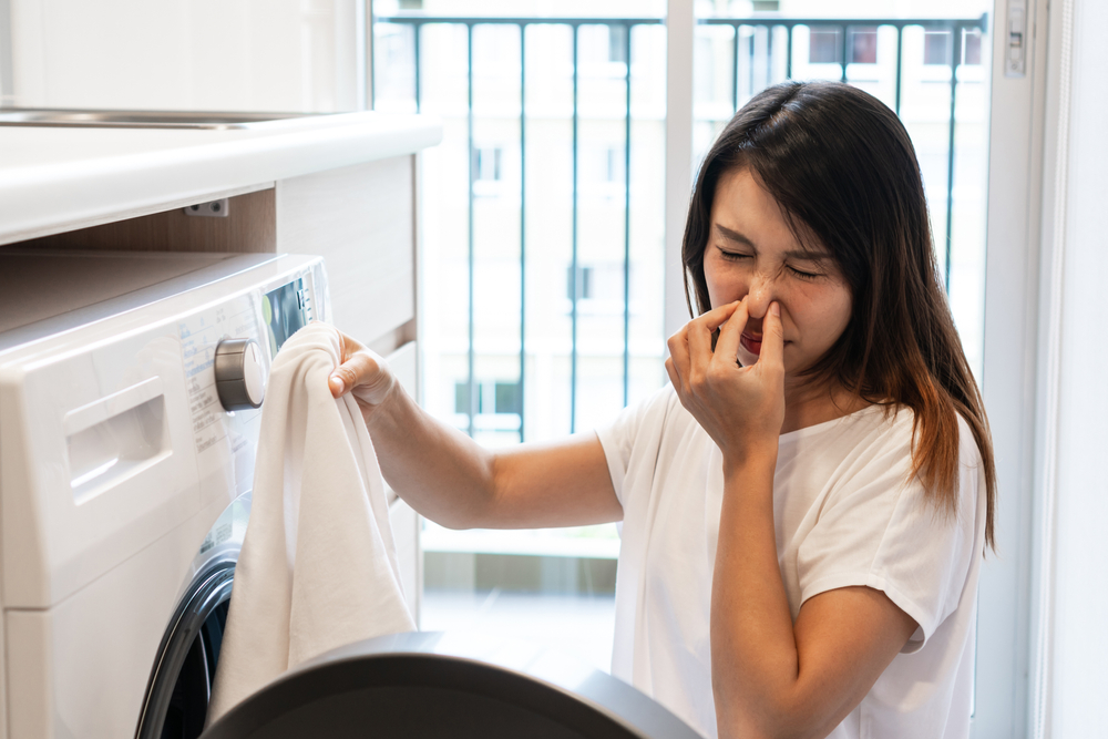 Washing machine stinks woman and smelling clothes after washing